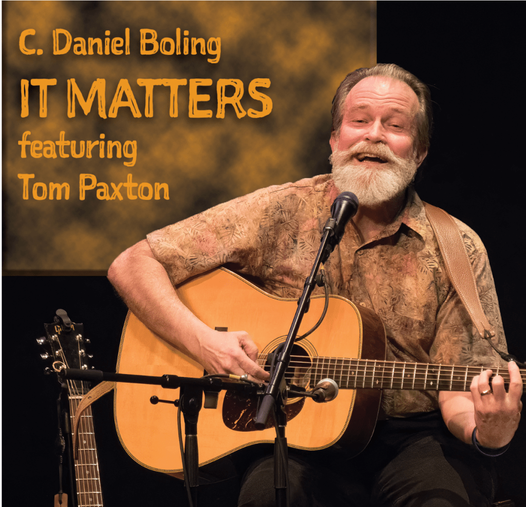 Smiling, bearded man playing an acoustic guitar