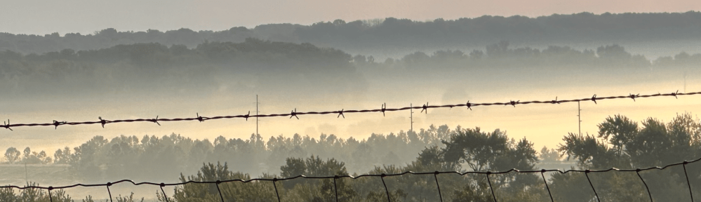 A misty valley looking through a barded wire fence