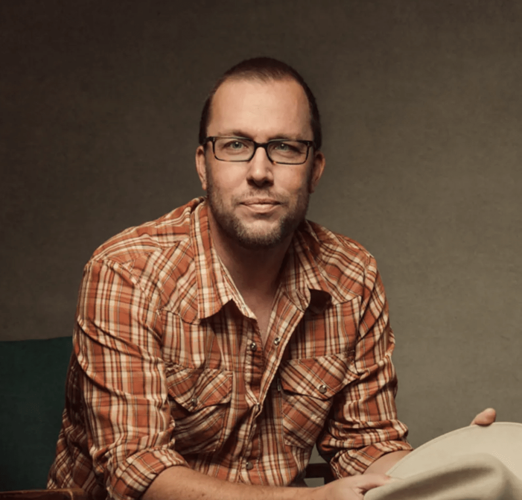 A man in a flannel shirt looks toward the camera. 