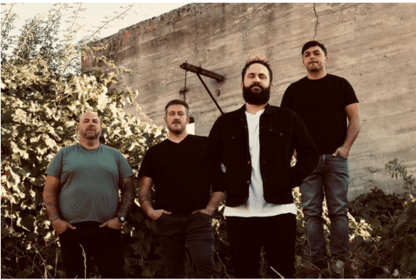 Four men stand in front of a cement wall.