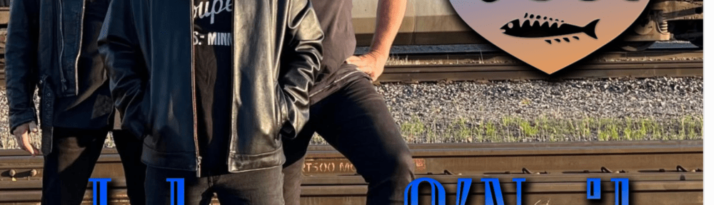 Three casually dressed men stand on a railroad track with a train on another track behind them.