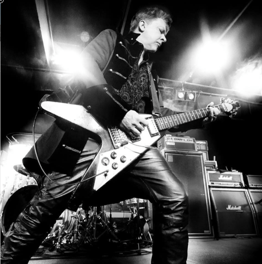 A man on a music stage playing a V- shaped electric guitar.