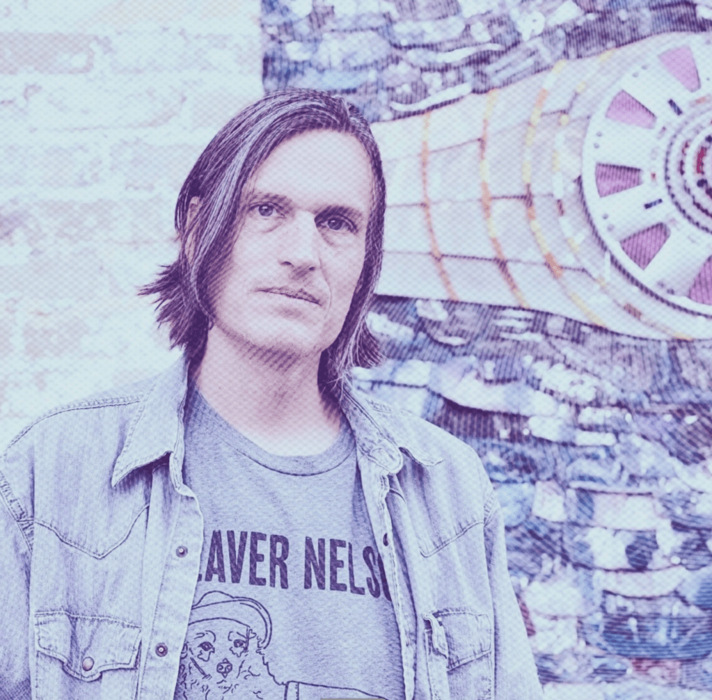 A casually dressed man with a serious expression looks out toward the viewer.