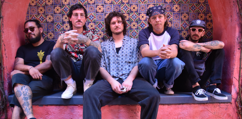 Five men sitting on a bench seat and looking toward the viewer. They are al casually dressed.