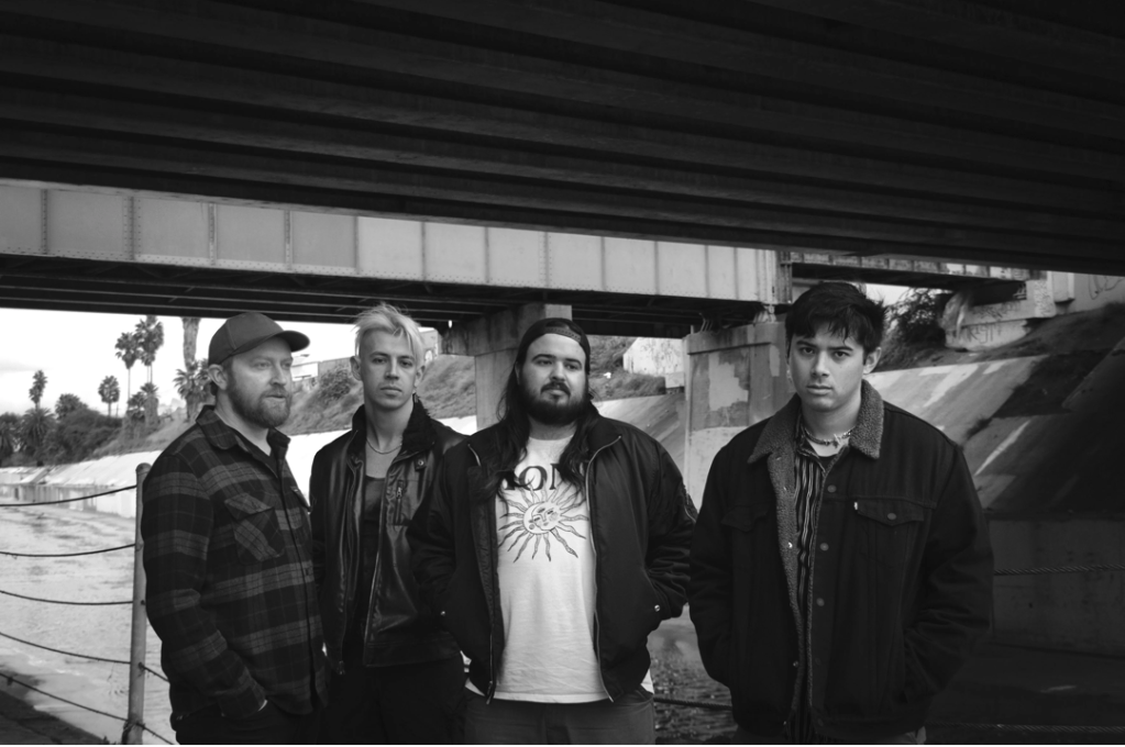 Four casually dressed men stand under a bridge. 