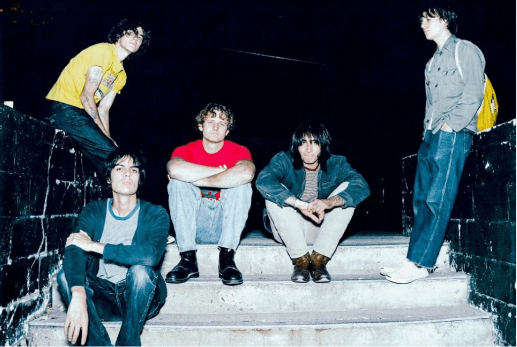 Five men sit on a cement stairs boarded by a black brick wall.  