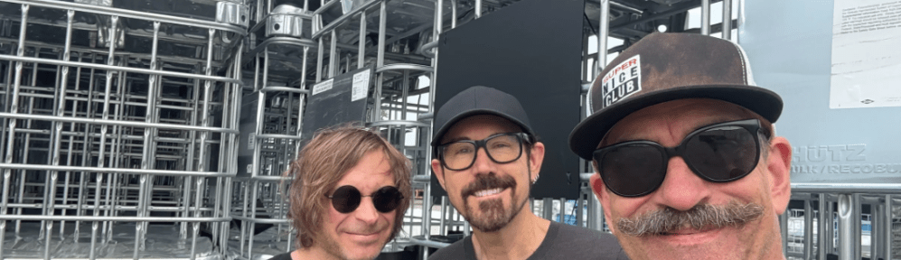 Three men stand looking toward the viewer. They appear to be happy.