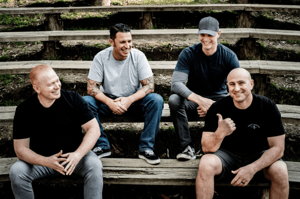 Four casually dressed men sitting on some tiered bench seating.  They seem to be happy.  