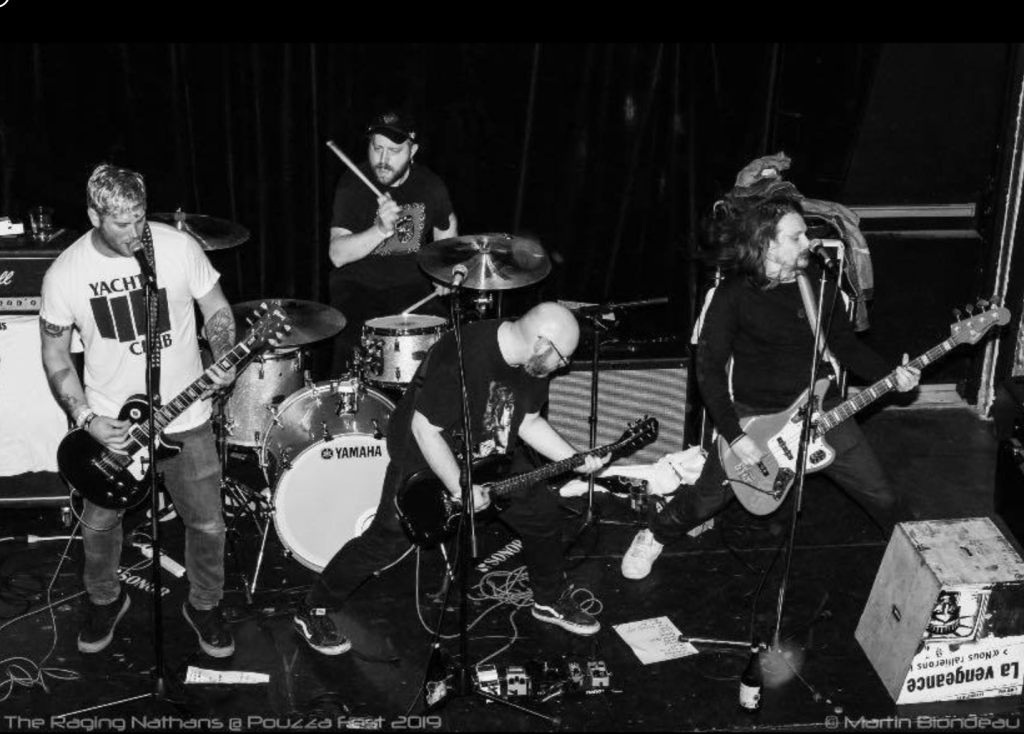A black and white photo of four male musicians playing music on a stage.  