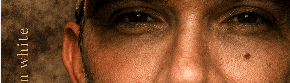 A close up image of a man in a baseball cap against a mottled brown background.