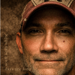 A close up image of a man in a baseball cap against a mottled brown background.