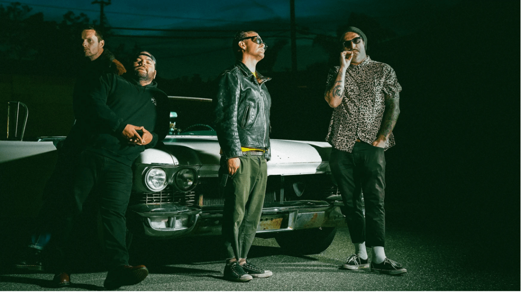 Four men standing around a classic convertible automobile.  The background is dark with low lighting in the foreground.